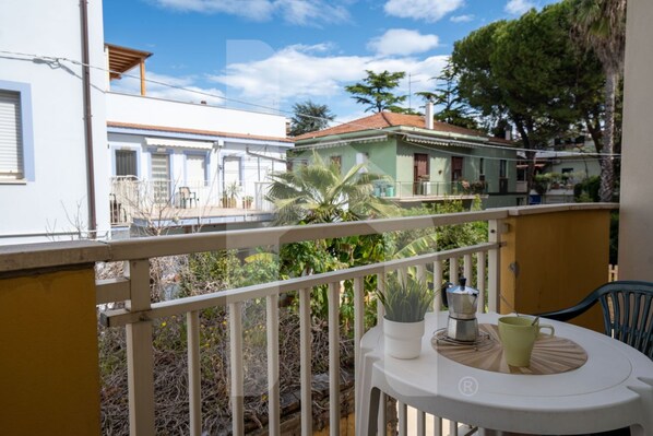 A balcony with a white railing, a table with a green mug, and a potted plant.