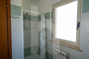 A bathroom with a shower, a window, and a radiator.