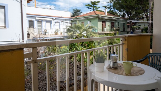 Ein Balkon mit einem weißen Tisch, einer grünen Tasse und einem Blumentopf.
