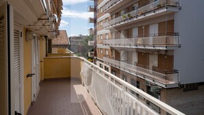 Un balcón estrecho con vistas a edificios vecinos, incluyendo un edificio de varios pisos con balcones.