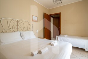 Quarto de hotel com duas camas, um quadro na parede e uma porta que dá para outro cômodo.