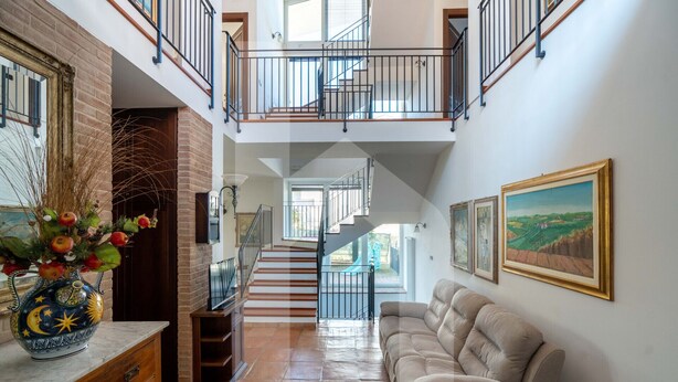 A spacious hallway with a staircase leading to an upper level, a beige sofa, and framed artwork on the walls. - Homiday - Villino Dei Poeti (Pineto)