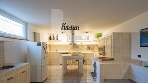 A modern kitchen with a central island, white cabinetry, and a 'Kitchen' sign above the island. - Homiday - Villino Dei Poeti (Pineto)