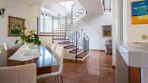 A dining area with a wooden table, white chairs, and a lace table runner. A staircase with a metal railing leads to an upper floor. - Homiday - Villino Dei Poeti (Pineto)