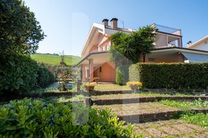 Une maison à deux étages dotée d’un balcon, entourée de haies bien entretenues et d’un jardin.