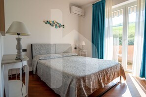 Une chambre à coucher comprenant un lit, une table de chevet, une lampe, un appareil de climatisation, un élément décoratif mural et une vue par une fenêtre avec des rideaux.