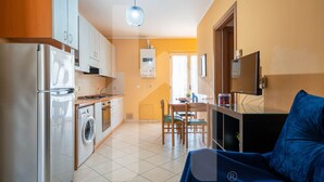 A compact kitchen with a washing machine, a dining area with a table and chairs, and a living area with a sofa and a TV. - Homiday - Via Gramsci Int.8, 3-room apartment on the 2nd Floor (Pineto)