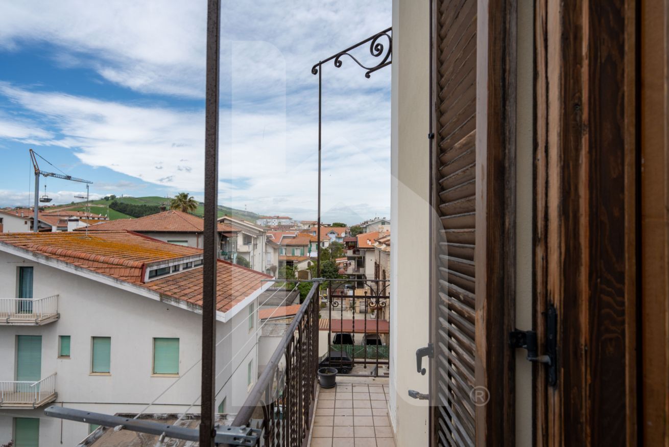 A balcony with a view of a residential area, a metal railing, and a wooden door.