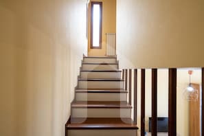 A staircase with wooden steps and a handrail, leading to a landing with a radiator and a window.