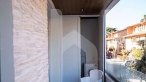 Un balcón moderno con un muro de piedra, una lavadora y dos sillas de mimbre.