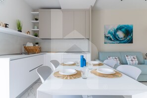 A modern kitchen with white cabinets, a dining table set with plates and cutlery, and a blue abstract painting on the wall.
