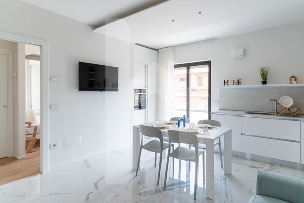 A modern kitchen with white cabinets, a built-in oven, and a dining area with a white table and chairs.