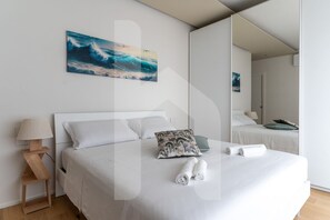 A modern hotel room with a large bed, a nightstand, a lamp, a painting of waves, and a mirror reflecting the room. - Homiday - Pinetina Residence Int. 05 (Pineto)