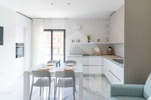 A modern kitchen with white cabinets, a dining table set for four, and a view to the outside. - Homiday - Pinetina Residence Int. 05 (Pineto)
