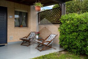 A covered patio area with two rocking chairs, a small table, and a potted plant. - In the heart of the Torre del Cerrano Marine Protected Area, a few steps from the beach is the Green Bay Village. The three-room apartment A01, on the mezzanine floor of the GRAN SASSO building, has an independent entrance with a small garden, pool view, (Pineto)