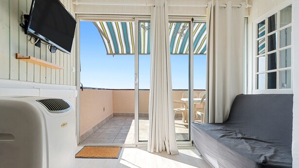 A room with a sofa, a TV mounted on the wall, a sliding glass door leading to an outdoor area with a table and chairs, and a ceiling fan. - Apartment 'Montsant' with Sea Views, Private Terrace and Air Conditioning (Creixell)