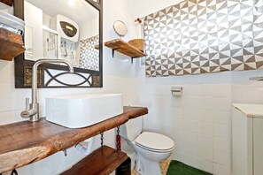 Un bagno con un mobile lavabo in legno, un lavandino bianco, un water, uno specchio e una tenda da doccia con motivo geometrico.