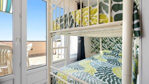 A bunk bed with a leaf-patterned bedspread, a white door, and a view of outdoor chairs and a table. - Apartment 'Montsant' with Sea Views, Private Terrace and Air Conditioning (Creixell)