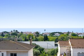 A residential area with terracotta-tiled roofs, a clear sky, and a view of the sea.