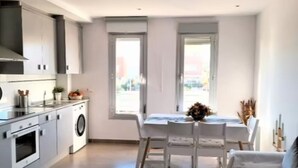 Een compacte keuken met moderne apparatuur, een zithoek met tafel en stoelen, en grote ramen die zorgen voor natuurlijk licht.
