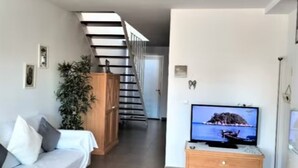 Een woonkamer met een bank, een televisie, een trap en een plant.
