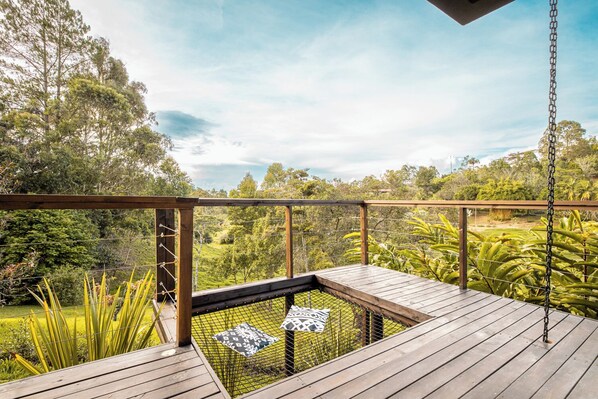A wooden deck with a metal railing, a swing, and a view of a lush landscape.