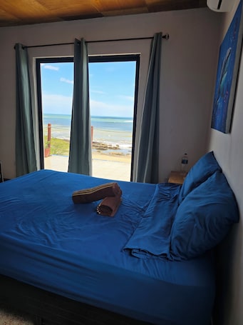 A bed with blue bedding, a rolled towel, and a pillow, with a view of the beach and ocean through a window.. Hotel Horizonte Azul