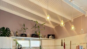 A kitchen with a white refrigerator, microwave, and sink. There are hanging pendant lights, a bar stool, and a potted plant.