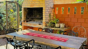 An outdoor patio with a brick oven, a table with chairs, and a wooden ceiling.