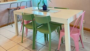 A dining area with a white table, green and pink chairs, and a hanging light fixture.