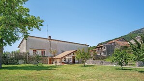 Un edificio de dos pisos con techo plano, un patio con mobiliario exterior y una pared de piedra.