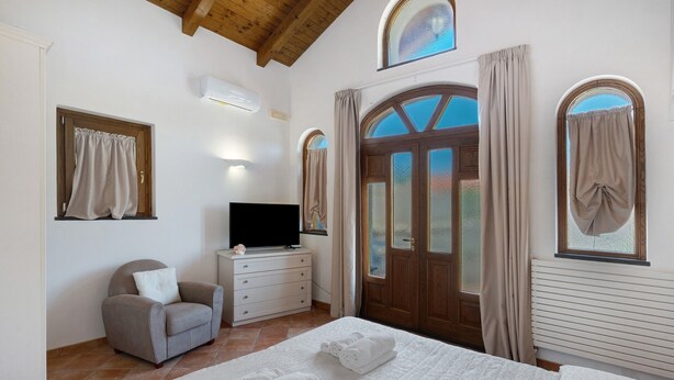 Un dormitorio con cama, una silla, un televisor y una puerta con ventanas.