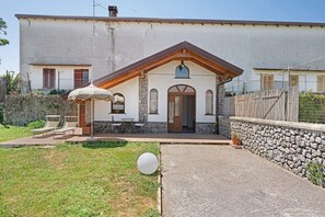 A two-story building with a stone facade, a wooden porch, and a small garden area with a white spherical object.