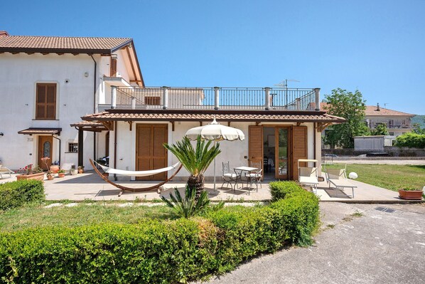 Une maison à deux étages dotée d’un balcon, d’un espace salon extérieur et d’un hamac.
