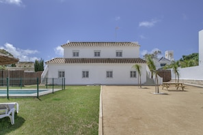 A two-story building with a tiled roof, a fenced swimming pool, and a sandy area.
