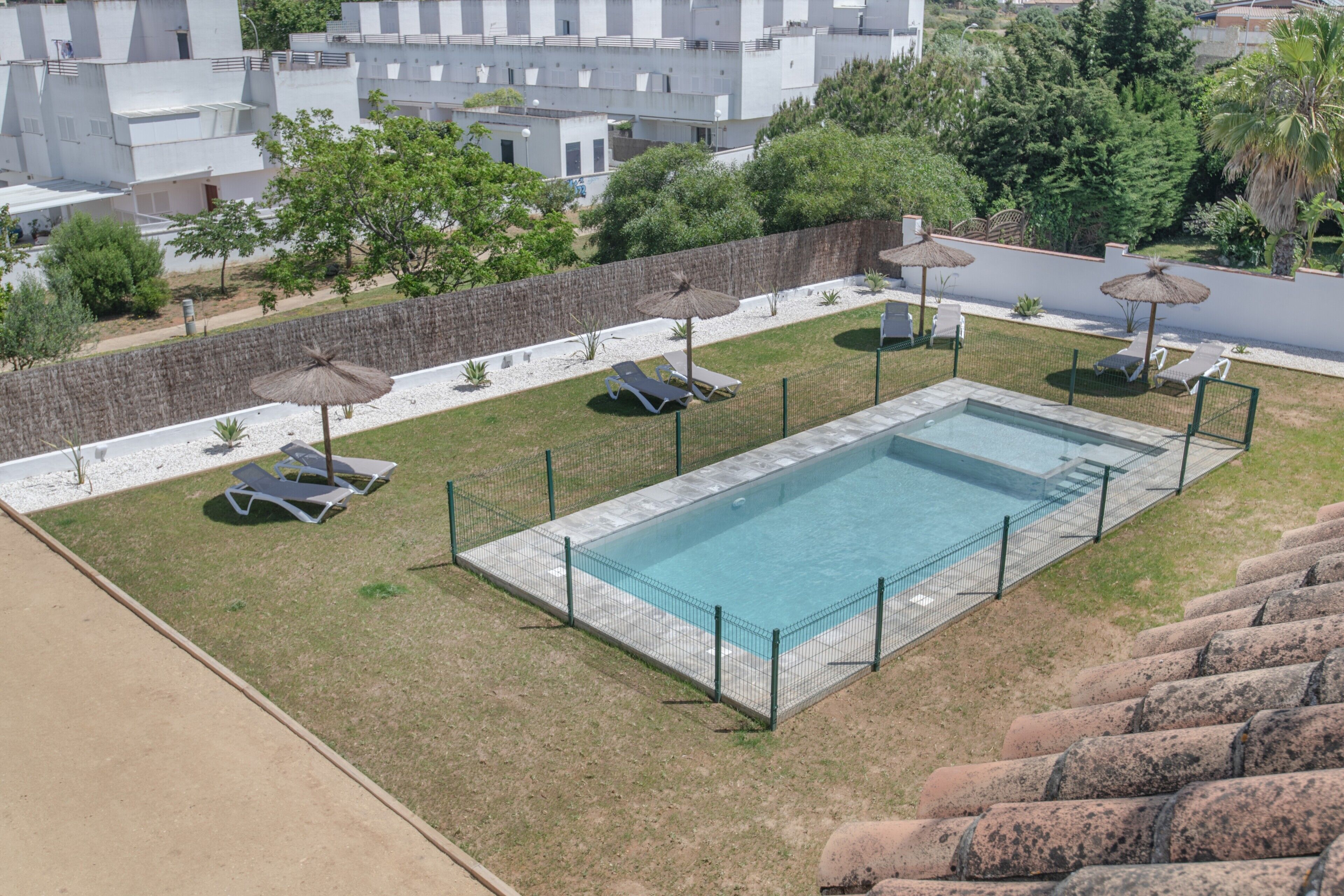 Una piscina rectangular con valla perimetral, tumbonas y sombrillas.