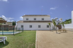 Un bâtiment à deux étages, doté d’un toit recouvert de tuiles, d’une piscine clôturée et d’un espace sablonneux.