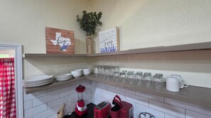 A kitchen with white tiled walls, a red toaster, a blender, and a coffee maker. There are shelves with plates, bowls, and glassware. - 3-bedroom house in charming Waco with WiFi, AC. Start your getaway (Waco)