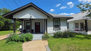 A single-story house with a front porch, a garage door, and a small garden area with flowers. - 3-bedroom house in charming Waco with WiFi, AC. Start your getaway (Waco)