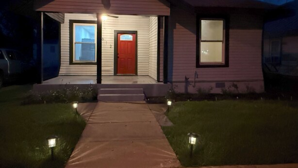 Una casa de dos pisos con una puerta roja, un porche delantero y un pequeño jardín frontal.