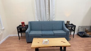 Una sala de estar con un sofá azul, una mesa de centro de madera, una mesita auxiliar negra con una lámpara, y una jaula para perro.