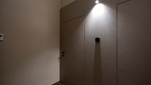 A closed door with a light fixture above it, a small device on the door, and a textured wall.