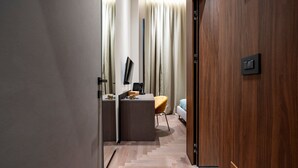 Une chambre d’hôtel moderne avec un plancher en bois, un bureau avec une chaise, un lit et un téléviseur fixé au mur.