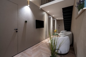 A hallway with a modern interior design, including a staircase, a mounted television, and seating area.