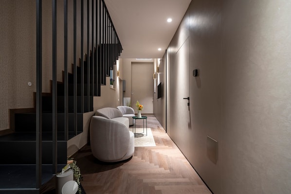 A modern interior with a staircase, a sofa, a small table with a vase, and a flat-screen TV mounted on the wall.