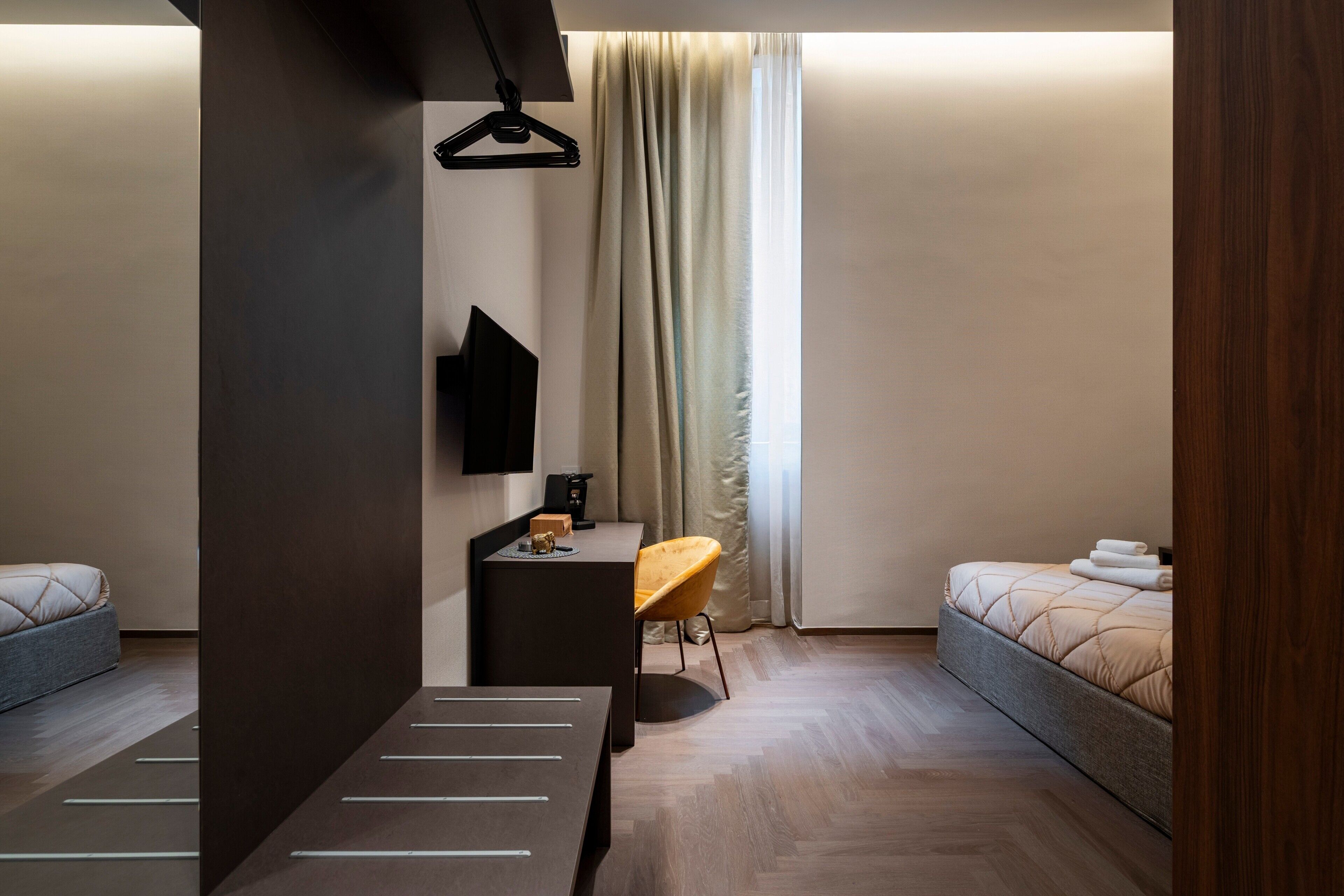 A modern hotel room with a bed, a desk, a chair, a TV, and a window with curtains.