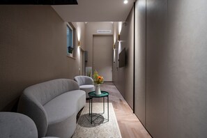 Un couloir étroit avec un canapé, une petite table sur laquelle est posé un vase de fleurs et un téléviseur fixé au mur.