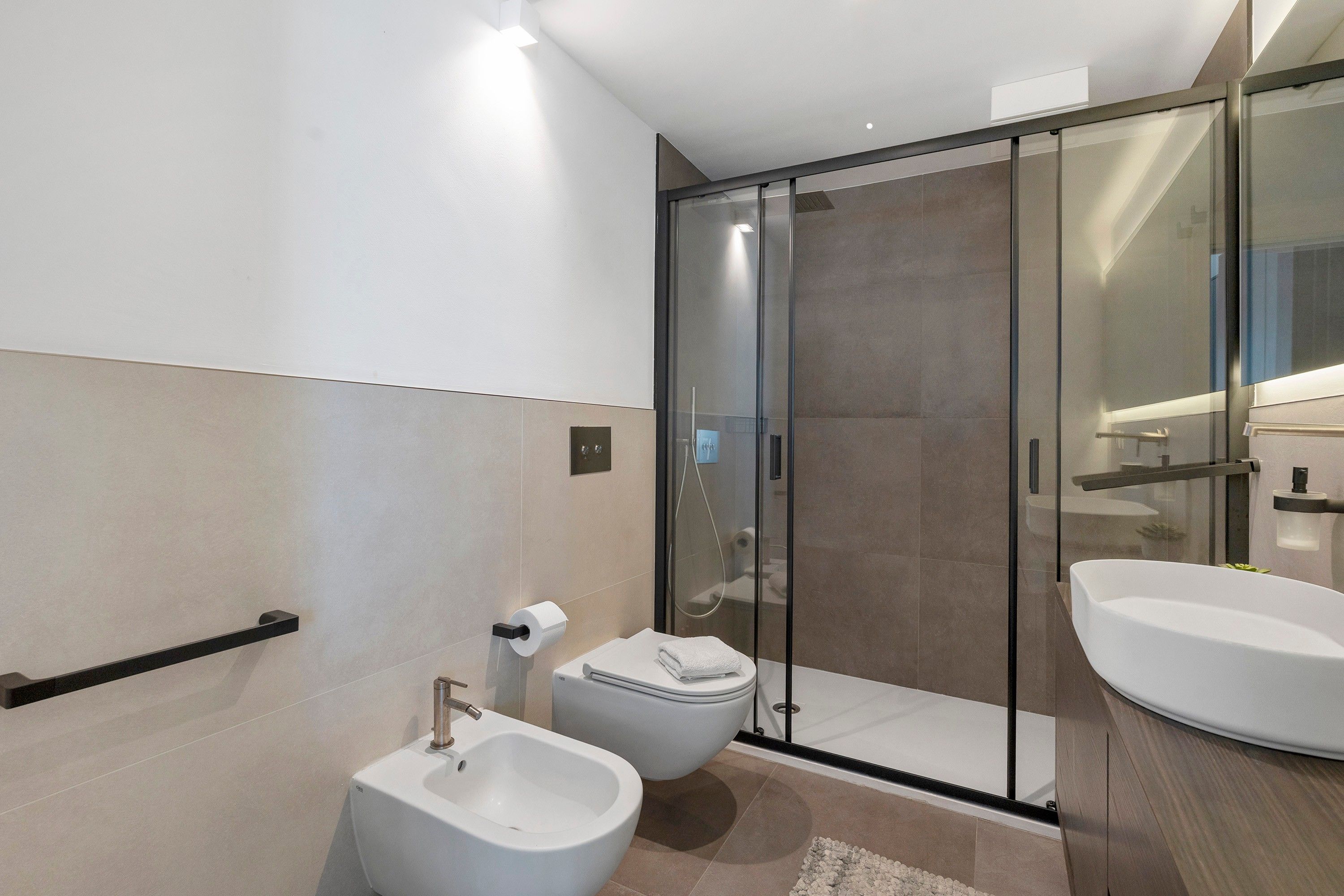 Un baño moderno con bidé, inodoro y ducha con mampara de vidrio.