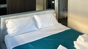 Una camera d'albergo con un letto, un armadio e un bagno visibile attraverso una porta aperta.