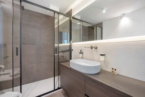 Un bagno moderno con cabina doccia in vetro, un lavandino bianco e un mobile bagno in legno.